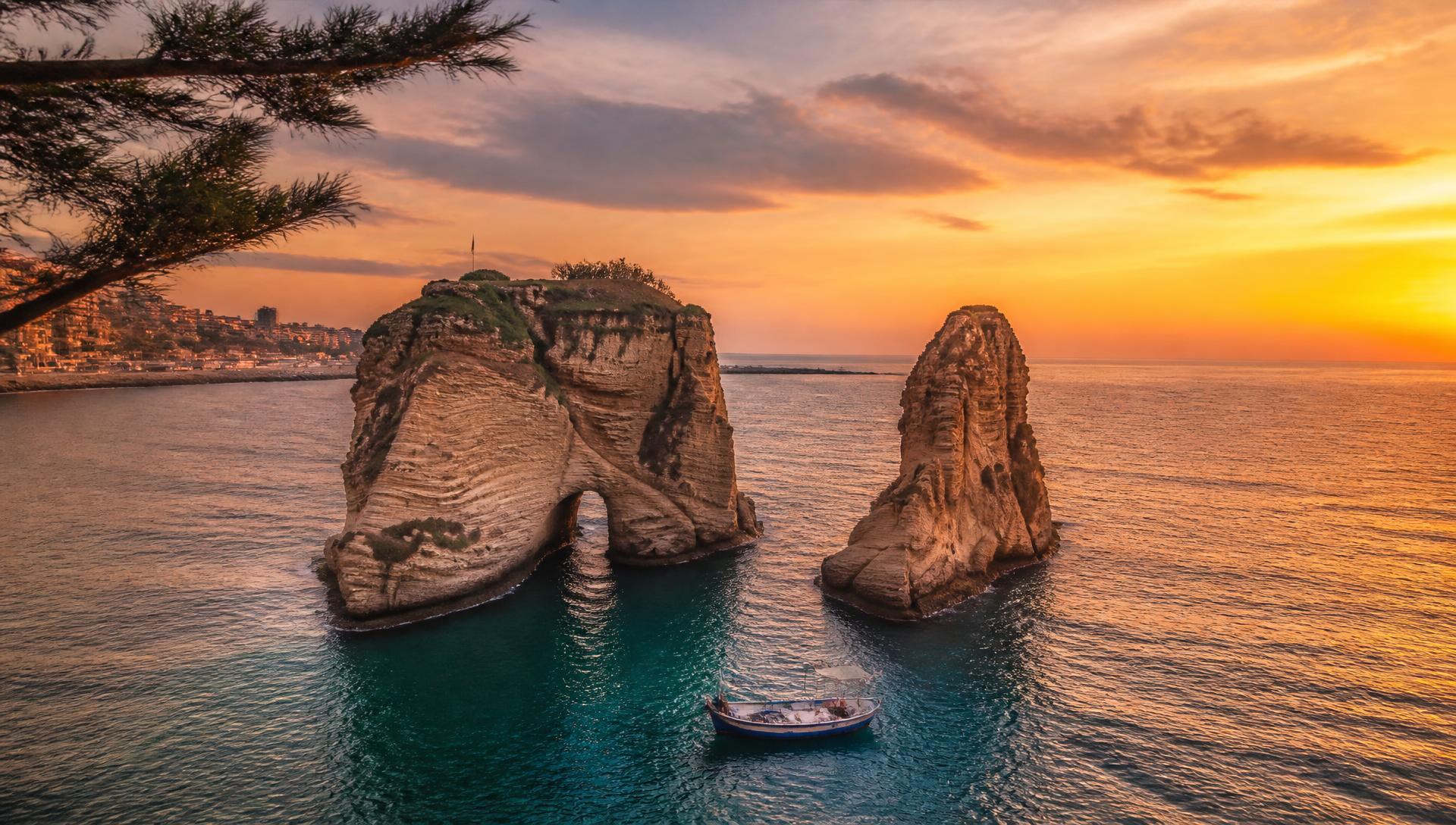 The famous Raouché rocks in Beirut at sunset, a traditional Lebanese fishing boat on the turquoise Mediterranean